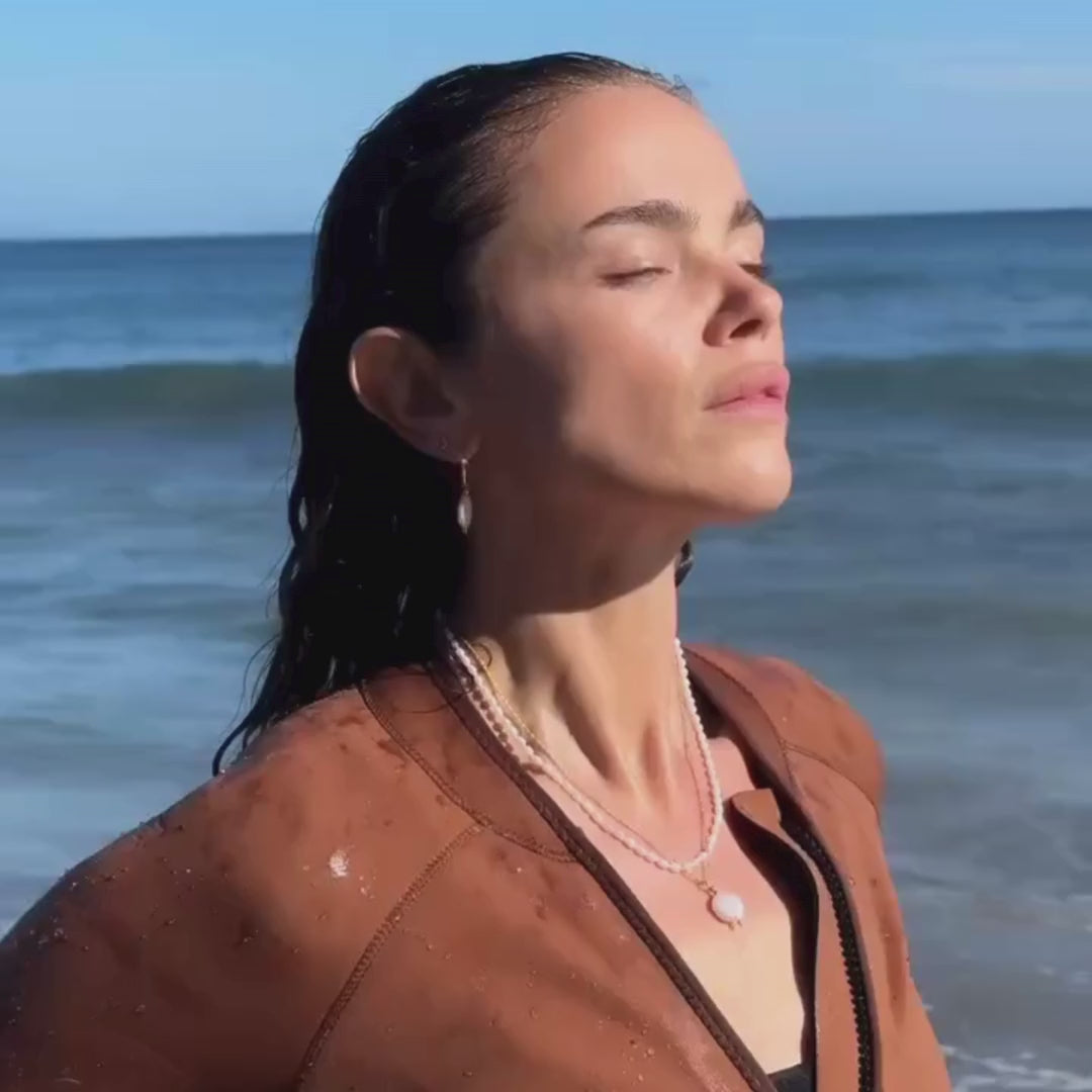 Video of a brown haired model wearing the Lily Blanche coin pearl set, necklace, bracelt and earrings, with a Fulmar wetsuit, emerging from the sea