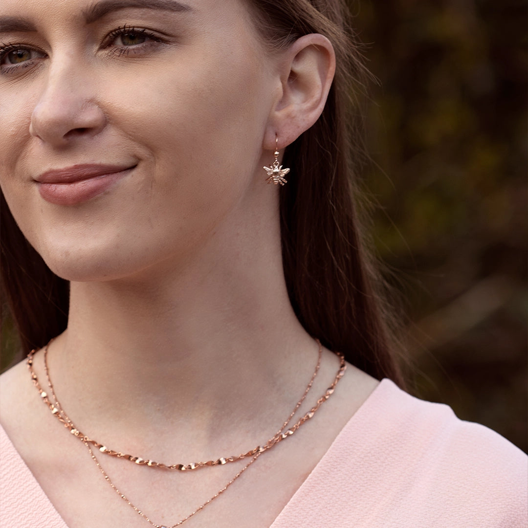 Model wearing rose gold bee drop earrings with layered rose gold necklaces, highlighting the intricate bee design and warm rose gold finish.