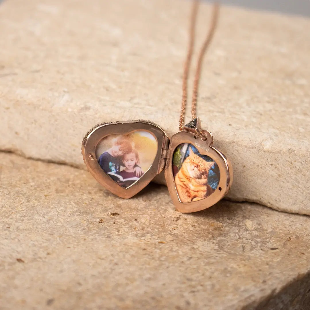 Rose gold heart locket necklace opened to reveal two personalised photo inserts, resting on a stone surface.