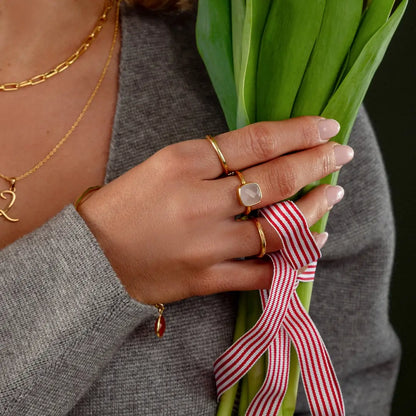 Gold ring with faceted rose quartz gemstone worn on hand holding green tulips with ribbon
