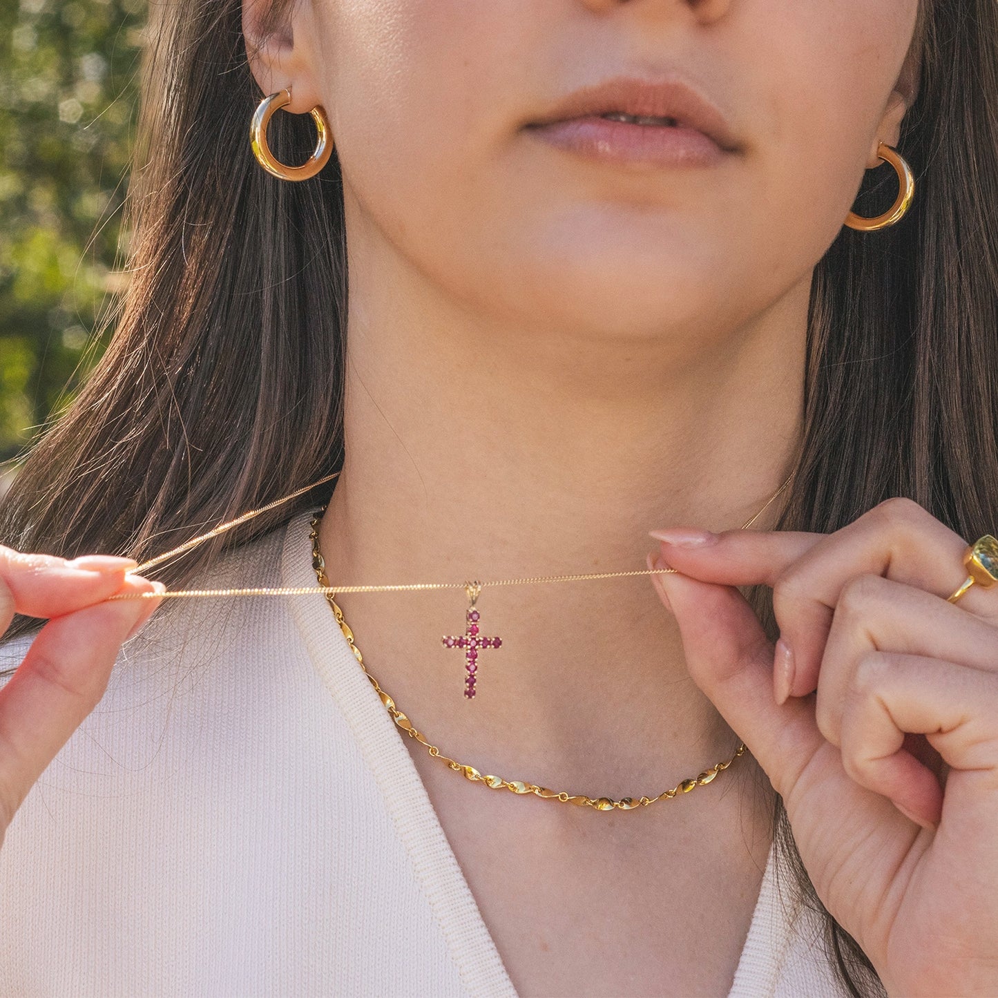 Close-up of a person wearing a gold necklace with a cross pendant, holding it with both hands.