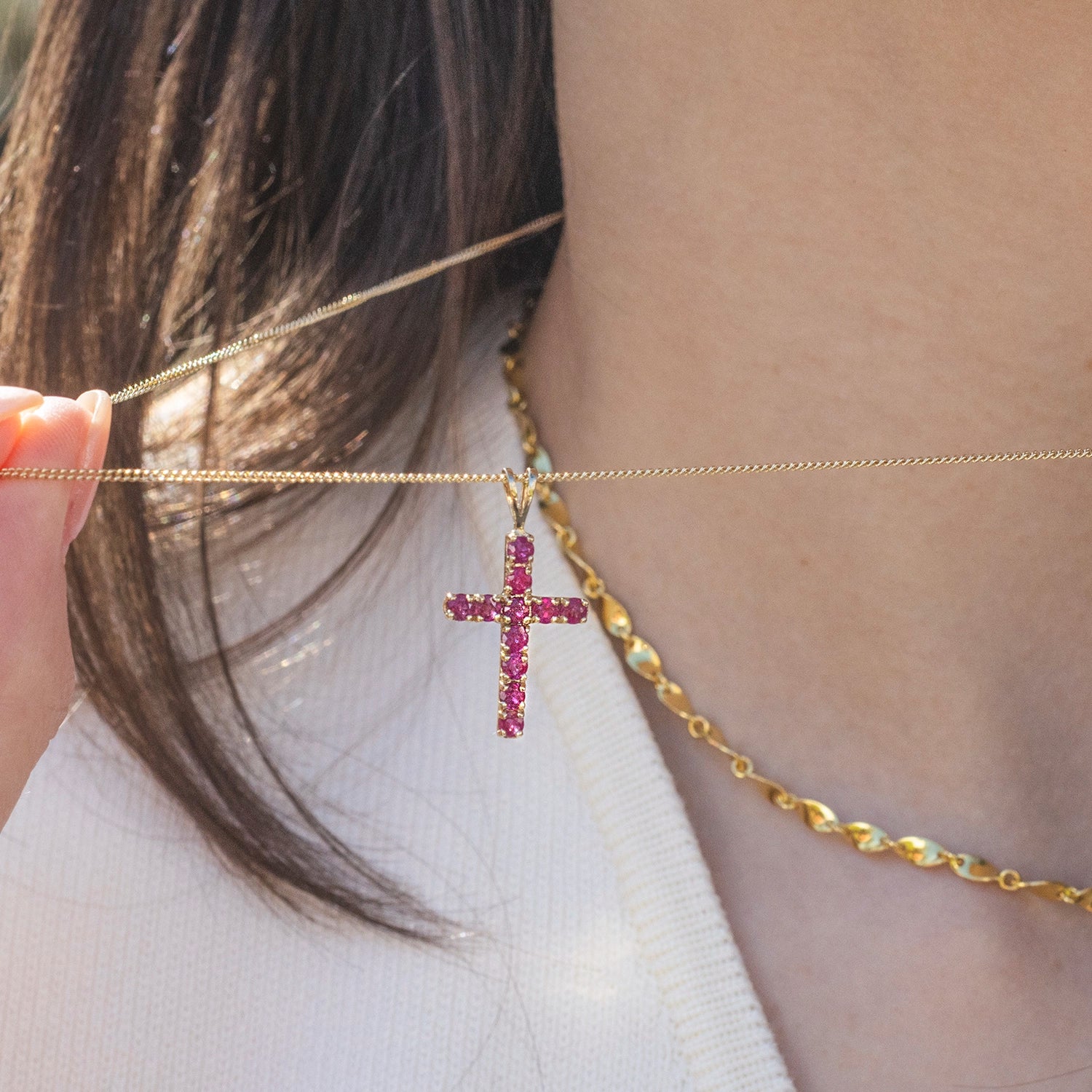 Gold chain with a ruby gemstone cross pendant worn by a person.