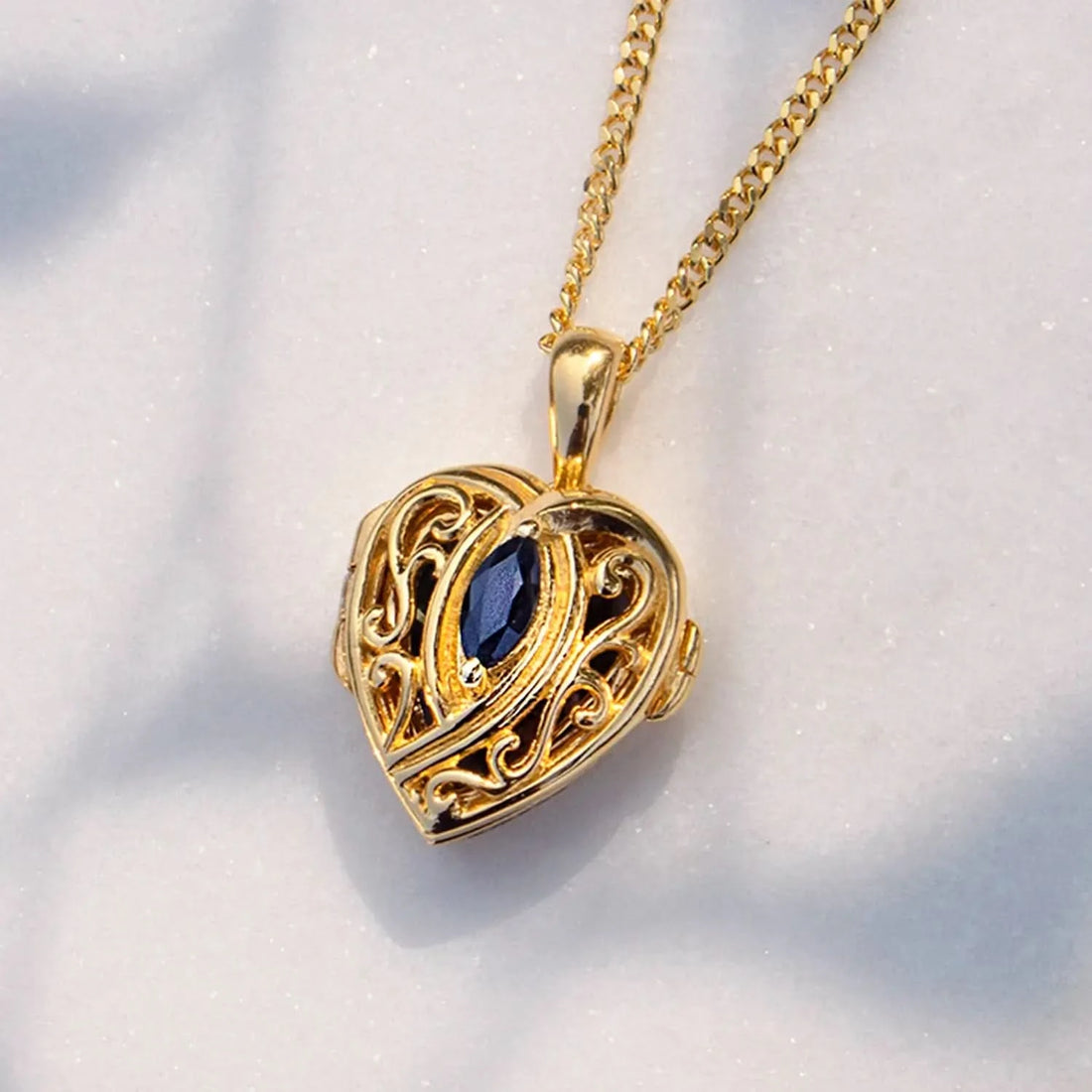 Gold heart locket necklace with filigree detail and blue sapphire gemstone