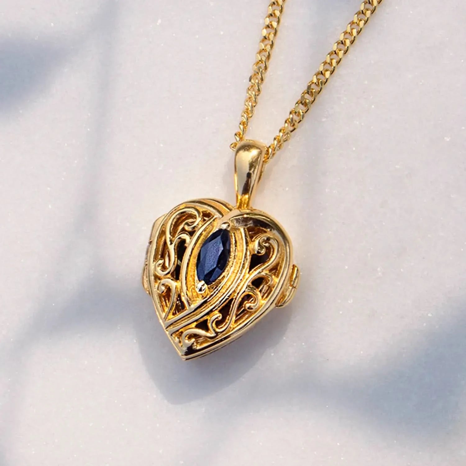 Gold heart locket necklace with filigree detail and blue sapphire gemstone