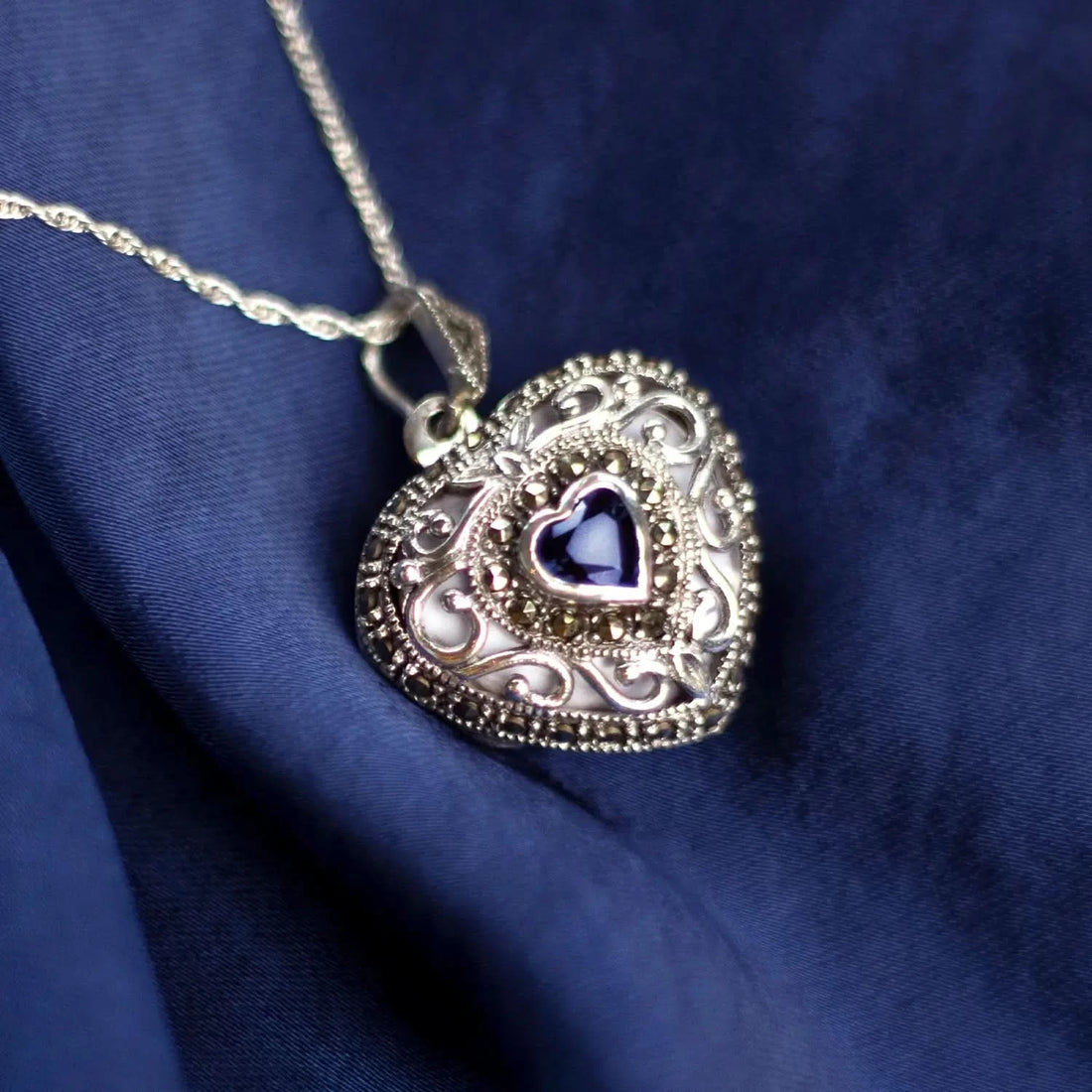Sapphire heart locket necklace in white gold with ornate filigree detail on blue fabric