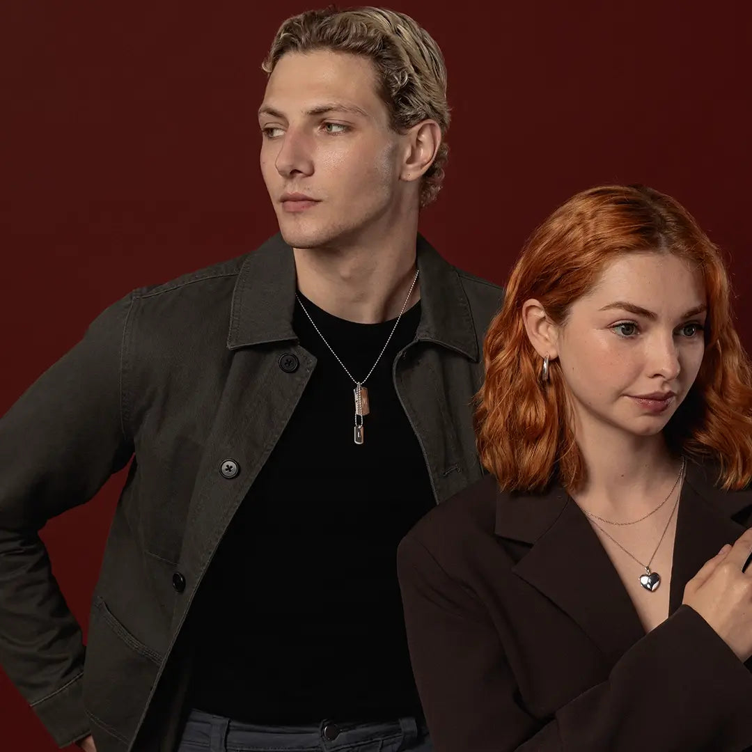 Male model wearing a silver double dog tag necklace alongside female model wearing a heart locket