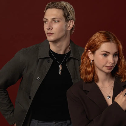 Male model wearing a silver double dog tag necklace alongside female model wearing a heart locket