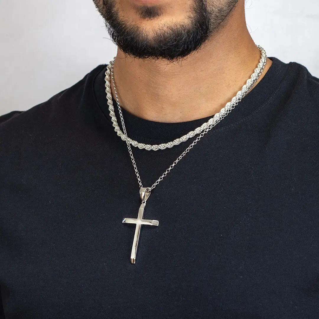close up of a man in a black T-shirt wearing  two silver necklaces, one with an XL cross pendant on a silver belcher chain and one a heavyweight rope chain