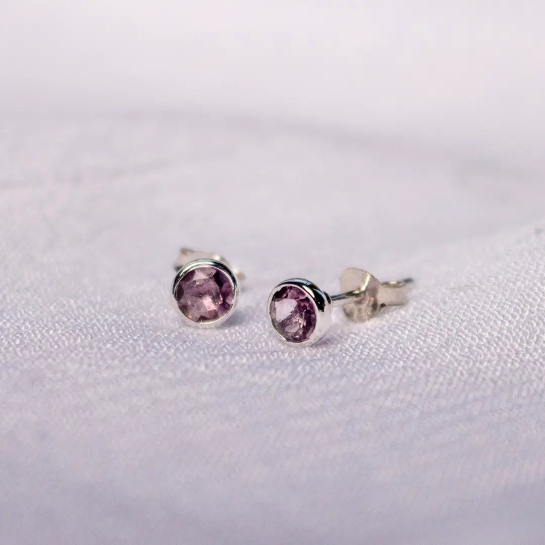 Sterling silver amethyst stud earrings with butterfly backs, featuring purple February birthstone gemstones on a textured white surface.