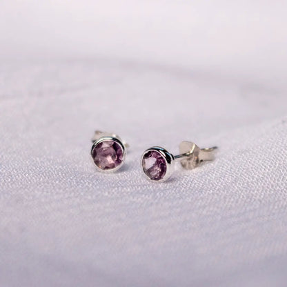 Sterling silver amethyst stud earrings with butterfly backs, featuring purple February birthstone gemstones on a textured white surface.
