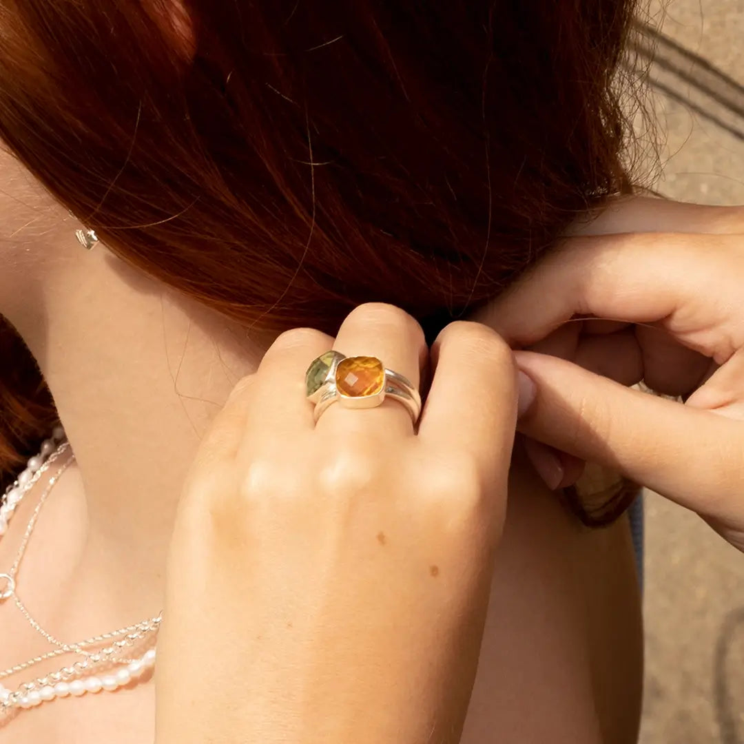 Two stacked rings with green amethyst and citrine gemstones worn on hand, styled with delicate silver and pearl necklaces