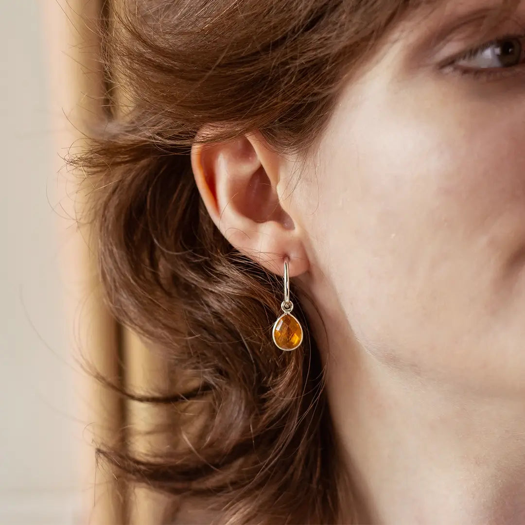 Close-up of a woman wearing a silver hoop earring with a teardrop-shaped citrine gemstone pendant.
