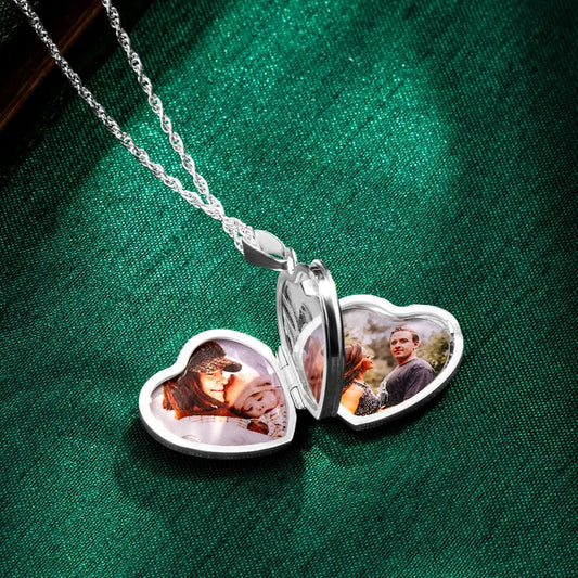 Open sterling silver heart locket necklace resting on green satin fabric, showing four personalised photo compartments inside the heart-shaped pendant.
