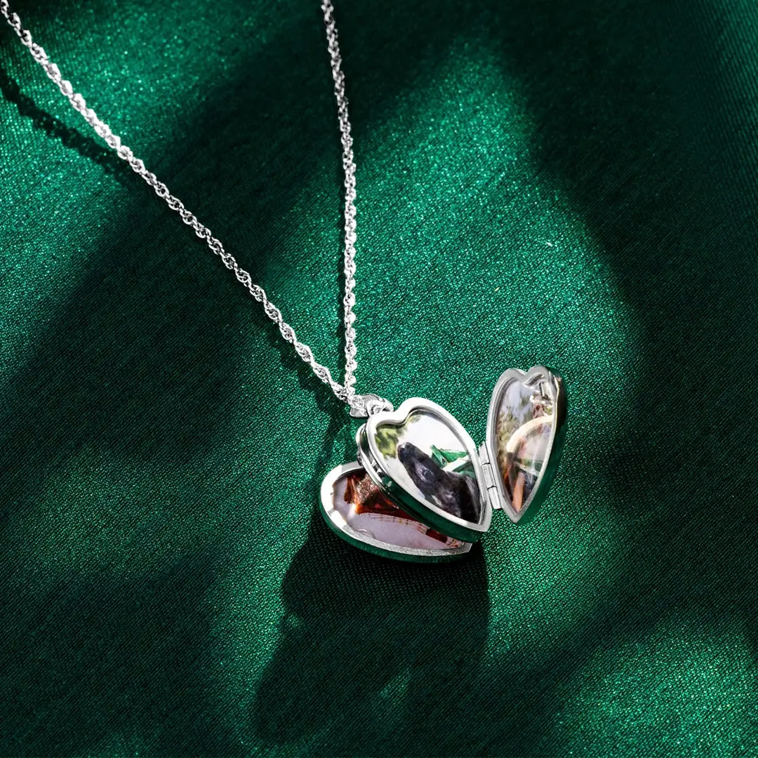 Open sterling silver heart locket necklace resting on green satin fabric, showing four personalised photo compartments inside the heart-shaped pendant.
