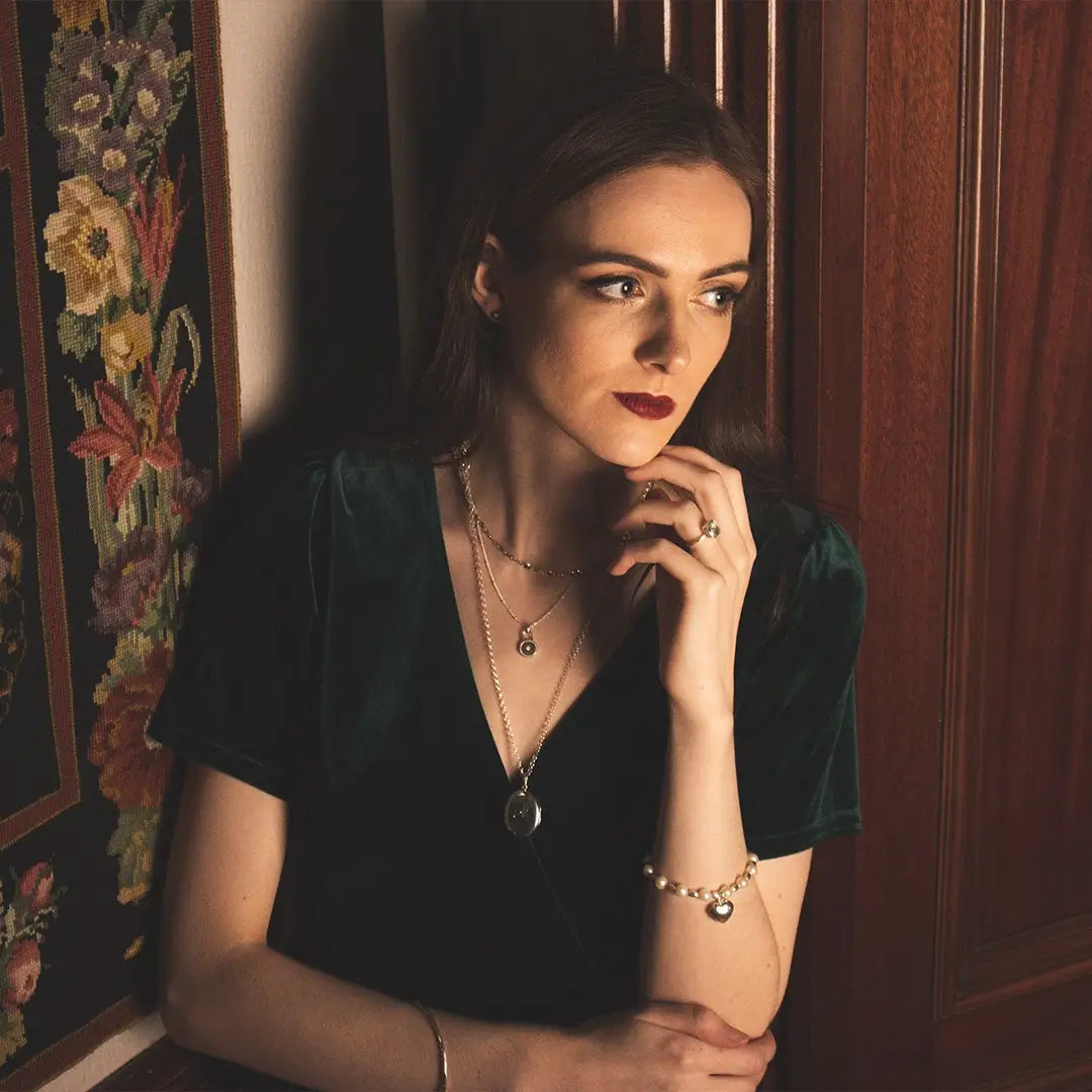 Woman wearing a sterling silver oval expanding photo locket necklace, styled elegantly against a wooden interior with soft, moody lighting.