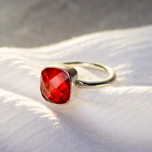 Sterling silver ring with faceted deep red garnet gemstone on soft fabric background