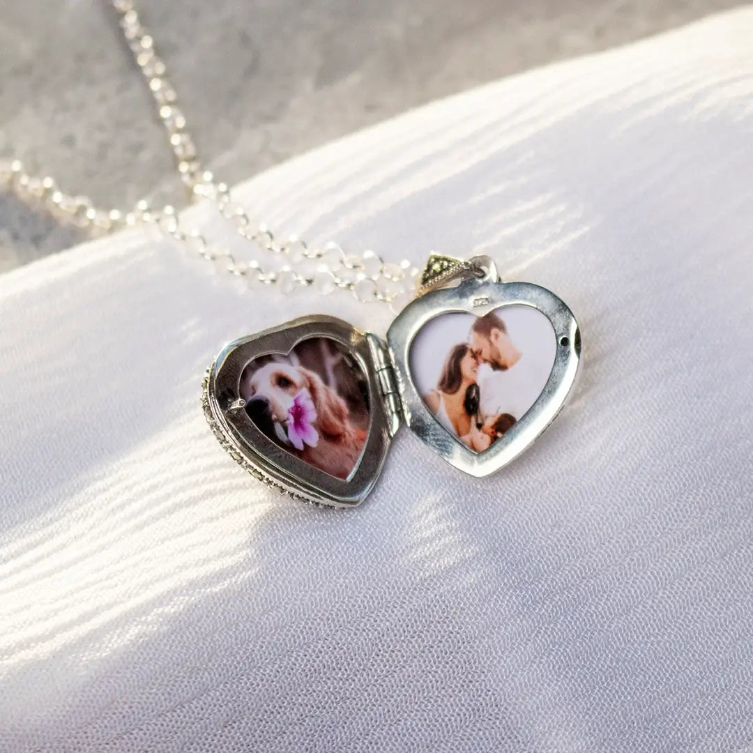 Open sterling silver heart locket necklace showing personalised photo inserts inside, displayed on white textured fabric with silver chain.