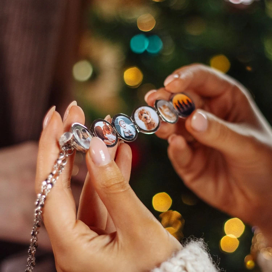 Model's hands holding an open sterling silver Memory Keeper Locket filled with six photos with blurred fairy lights in the background