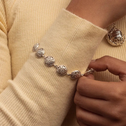 Sterling silver Memory Keeper bracelet with ornate filigree circular links, worn on a wrist with a soft yellow knit sweater, hand gently adjusting the clasp
