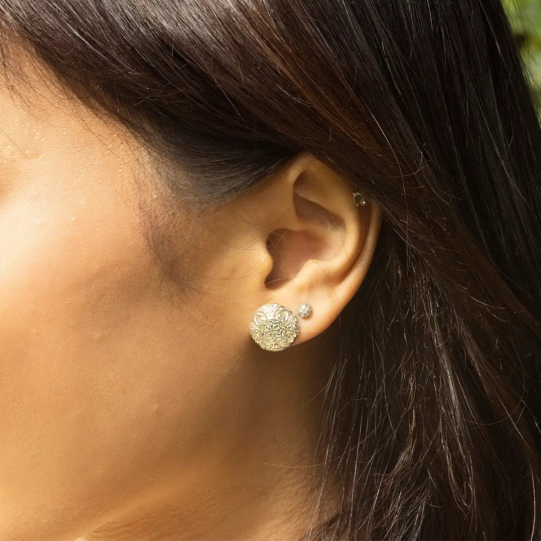 Close-up of sterling silver filigree design stud earrings on ear, paired with a small crystal stud, showcasing detailed craftsmanship and texture.