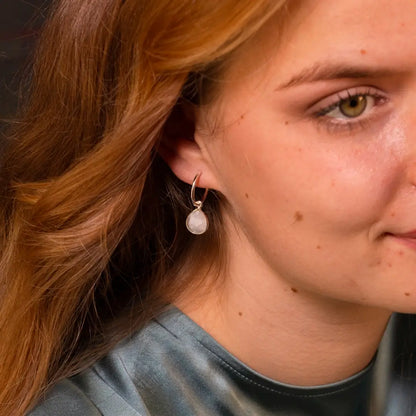 Close-up of a woman wearing silver hoop earrings with round moonstone gemstone drops, paired with a teal satin blouse