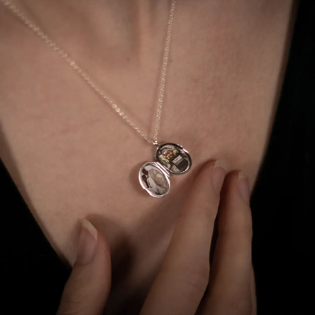 Close-up of an open sterling silver oval diamond photo locket showing personalised photographs inside, worn on a fine silver chain.