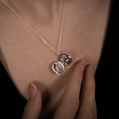Close-up of an open sterling silver oval diamond photo locket showing personalised photographs inside, worn on a fine silver chain.