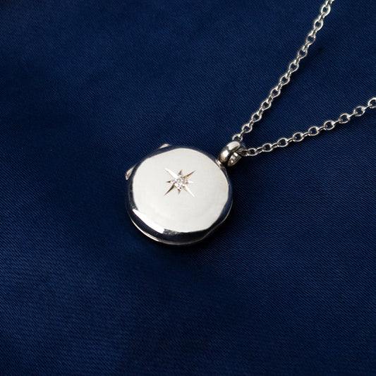 small round diamond locket in silver on a piece of blue fabric