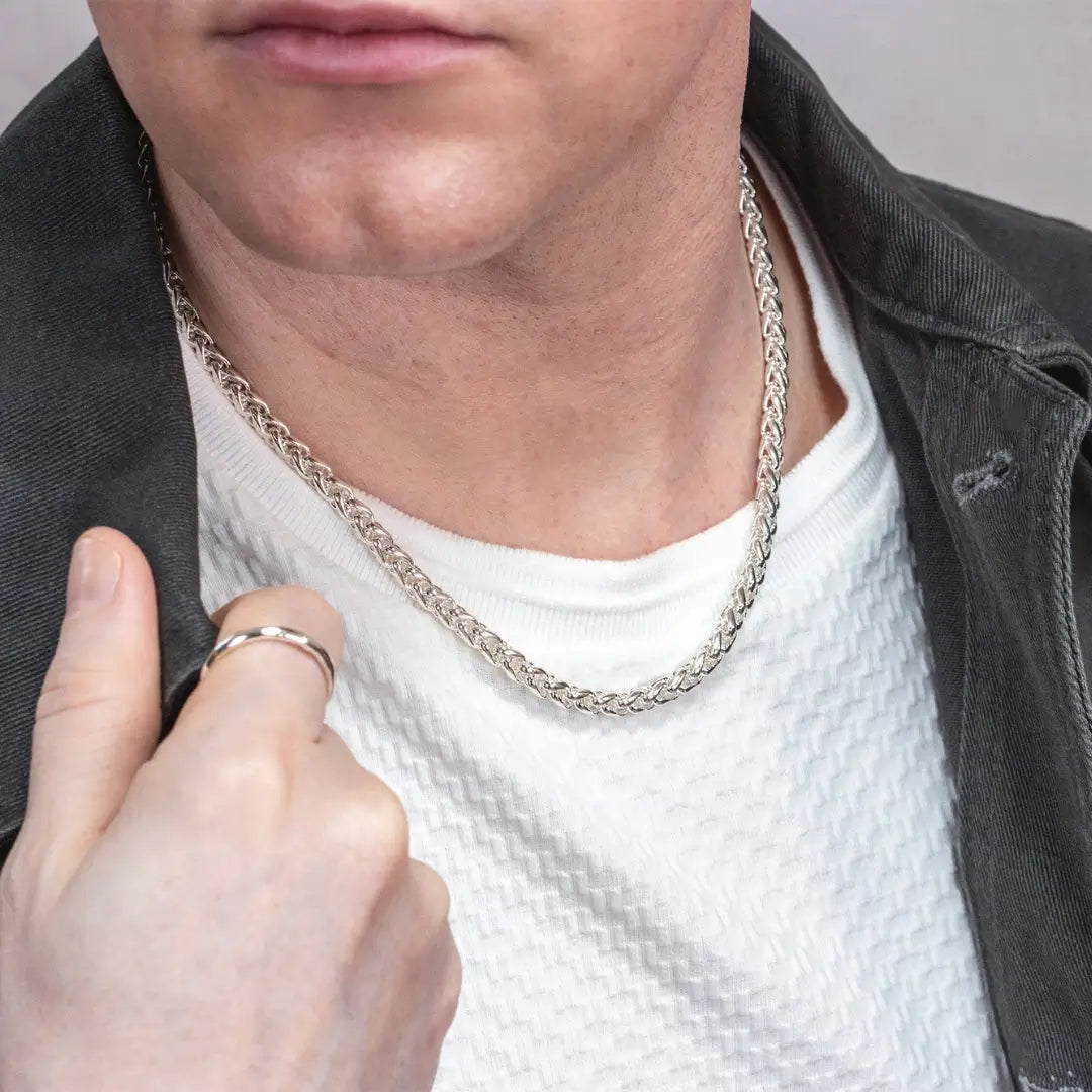 Man wearing a sterling silver spiga chain necklace with a white textured shirt and dark jacket.