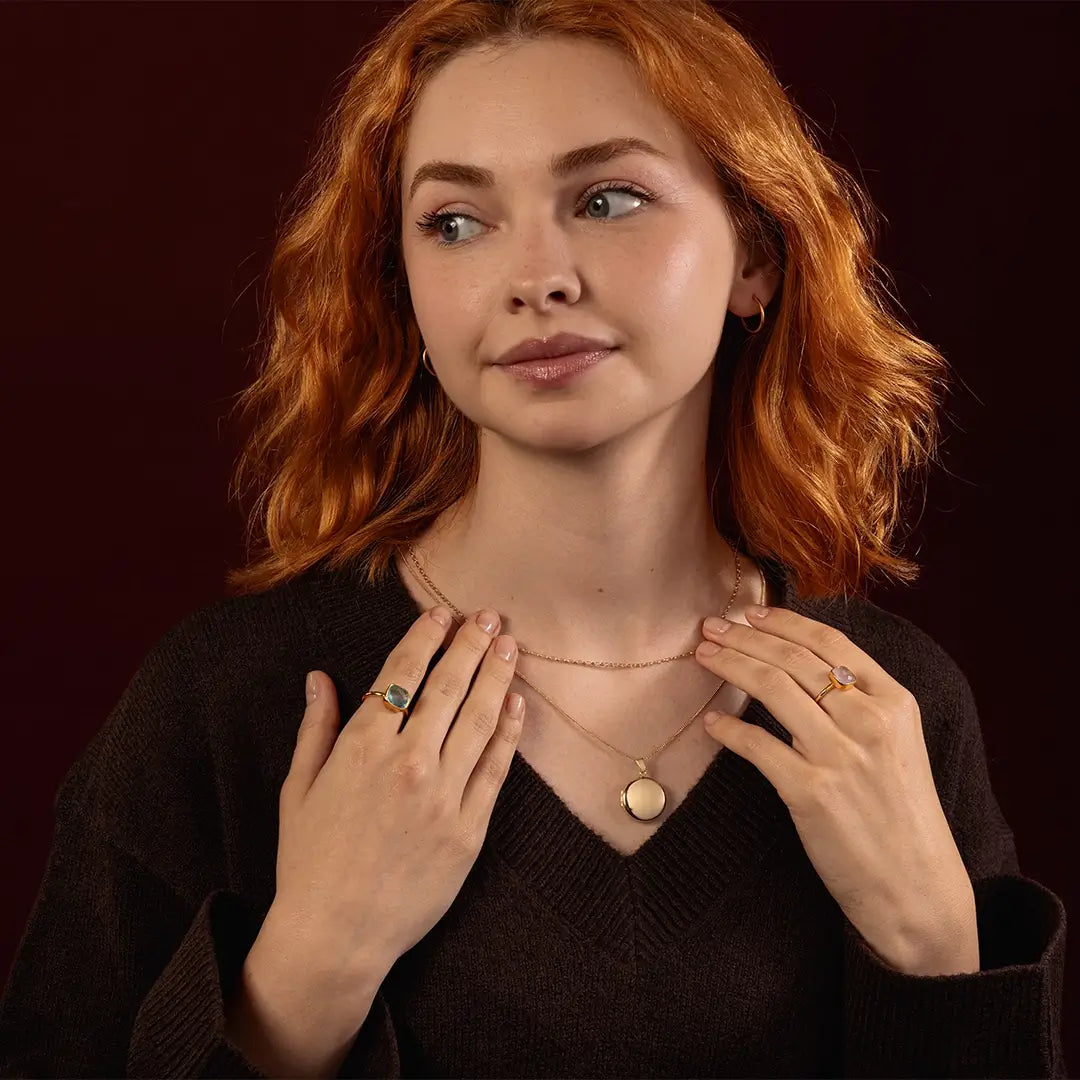 Model wearing a solid 9ct gold round locket necklace layered with gold jewellery