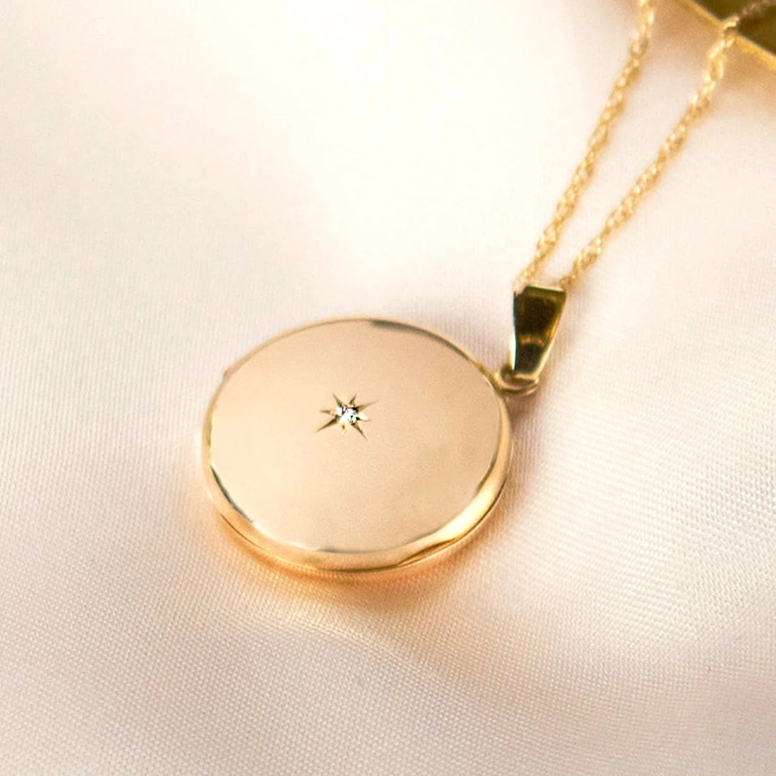 round diamond locket in gold next to gold plate