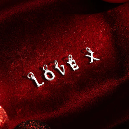 White gold letter charms spelling “LOVE X” displayed on deep red velvet fabric,