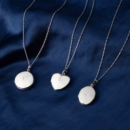 Solid White Gold round, heart and oval lockets with star detail on fine chains, displayed on navy fabric background