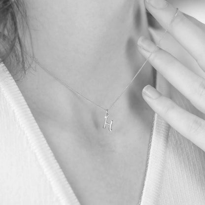 Person wearing a white gold necklace with a 'H' pendant, close-up of the necklace.