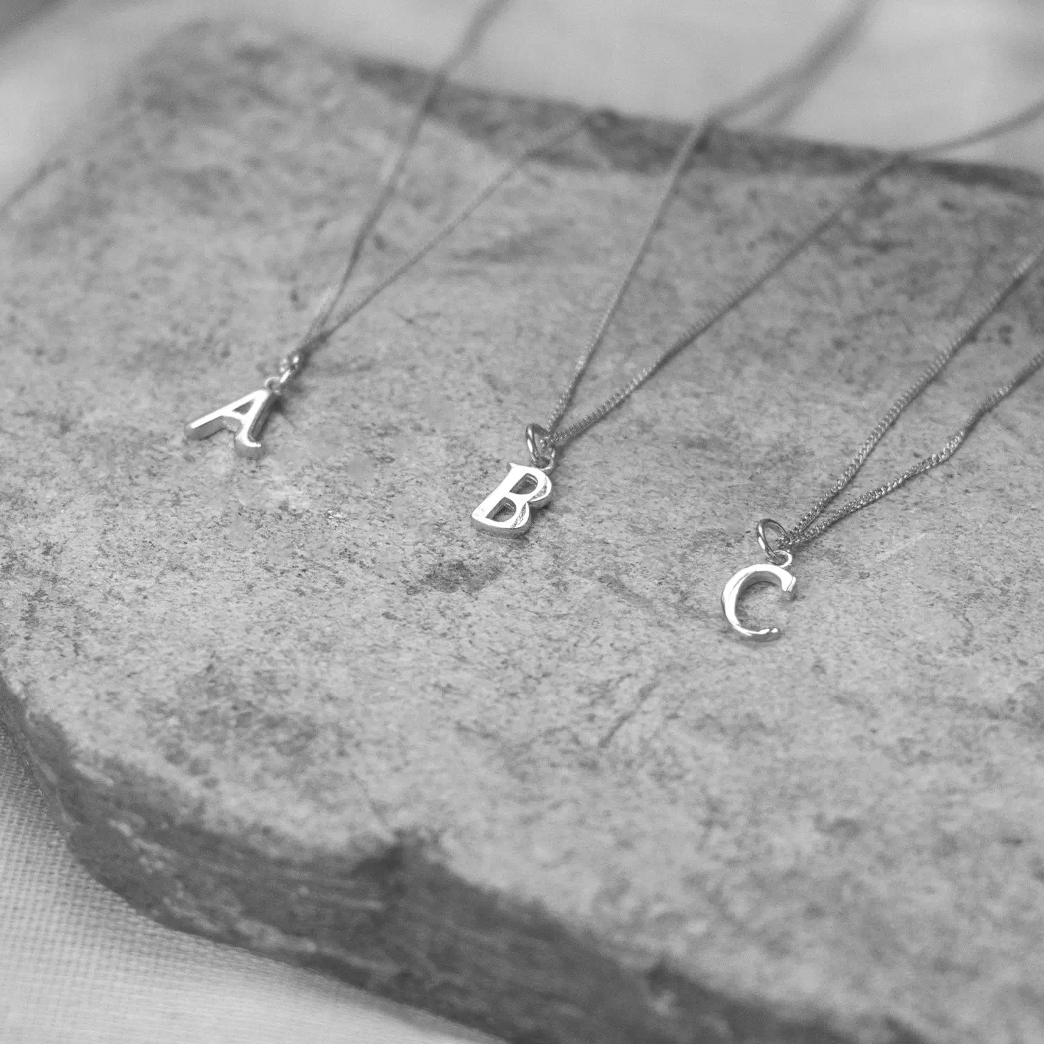 Three white gold necklaces with letter pendants on a stone surface