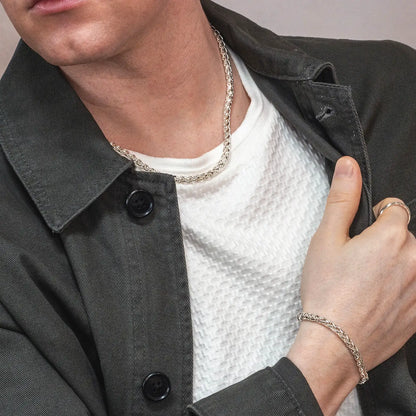 Person wearing a sterling silver heavyweight men's Spiga chain necklace and bracelet with a black jacket and white shirt.