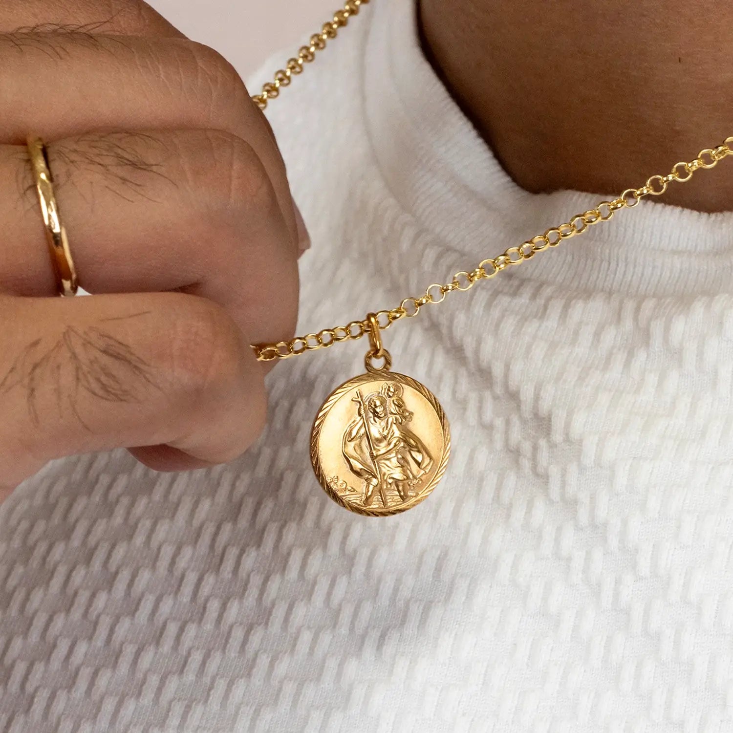 Gold st Christopher necklace with a pendant held by a hand on a neutral background