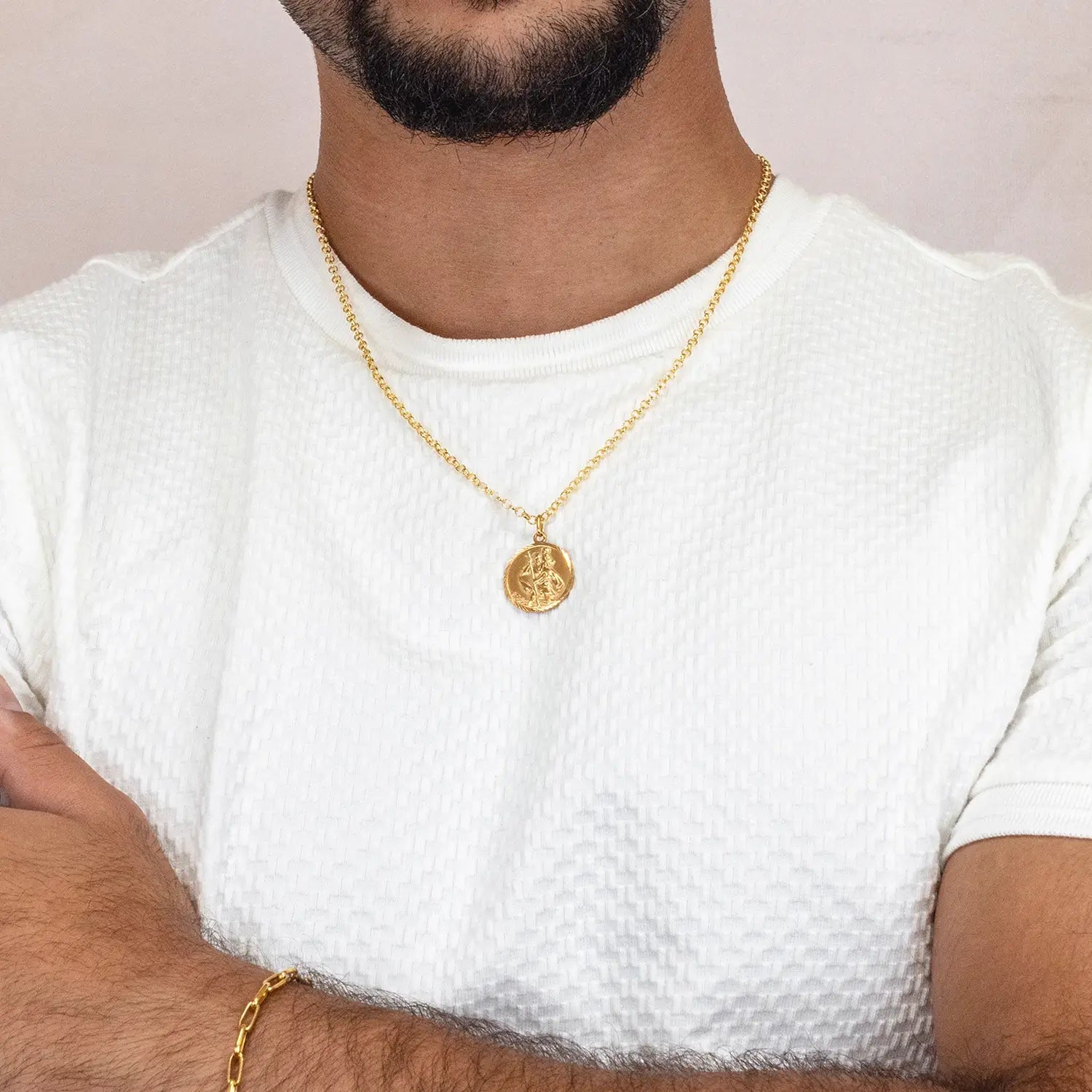 Man wearing a gold st Christopher necklace with a pendant on a plain background