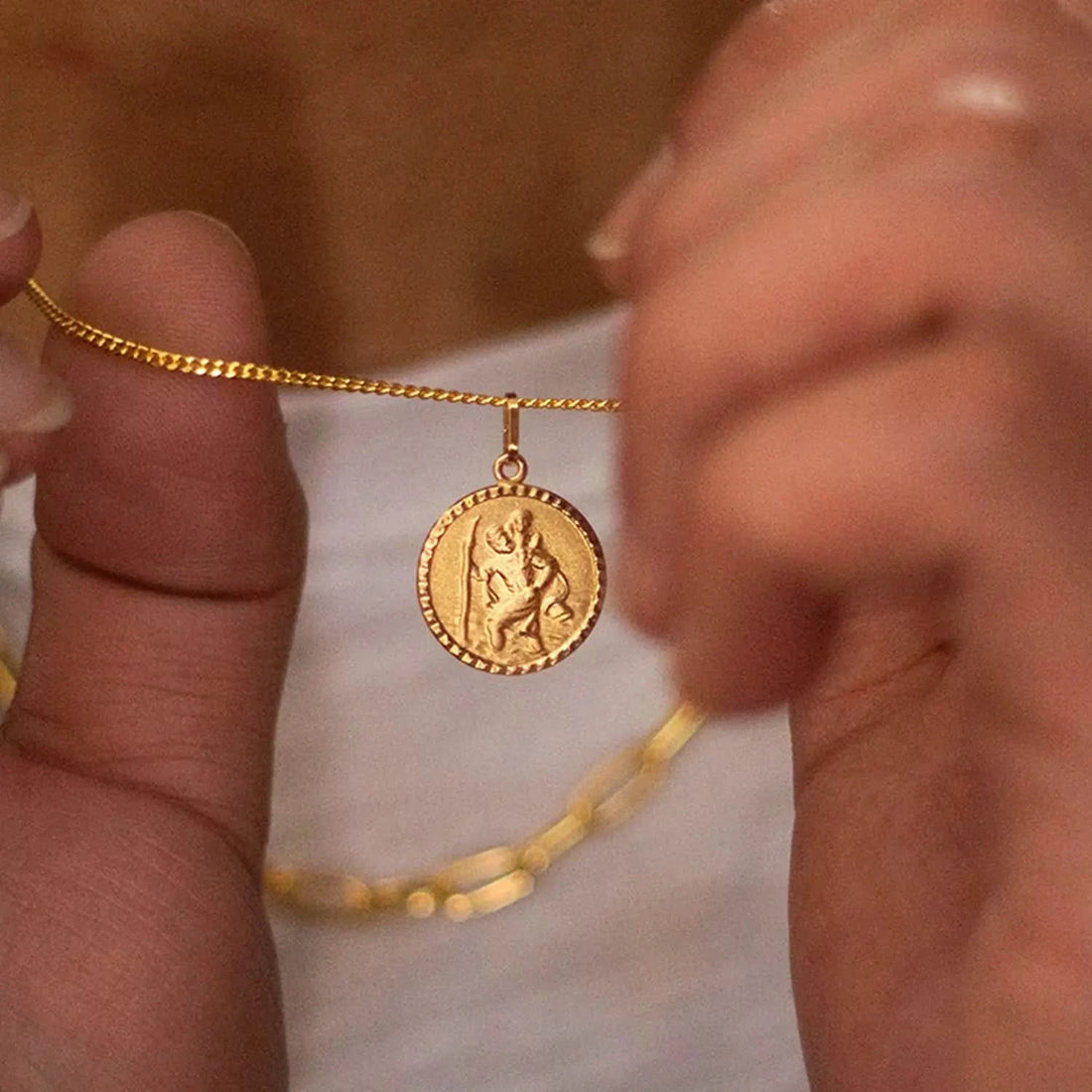 photograph a gold St. Christopher necklace. The round medallion pendant features intricate engraved details of the patron saint of travel, paired with a delicate chain