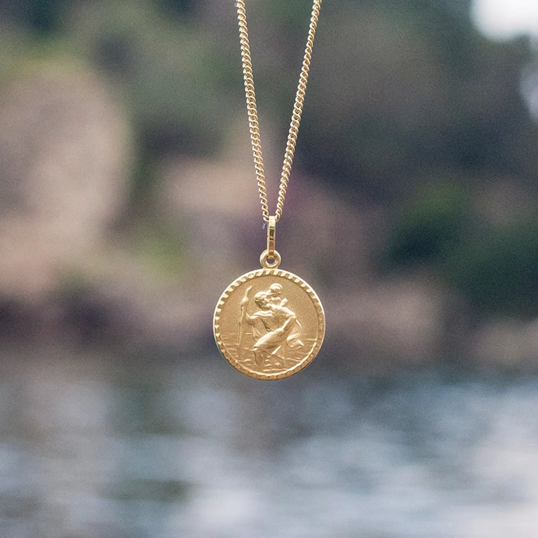 photograph of a gold st Christopher necklace against a sea background