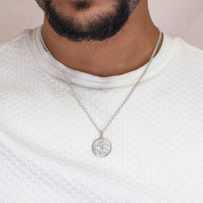 Man wearing a silver st Christopher necklace with a pendant on a plain background