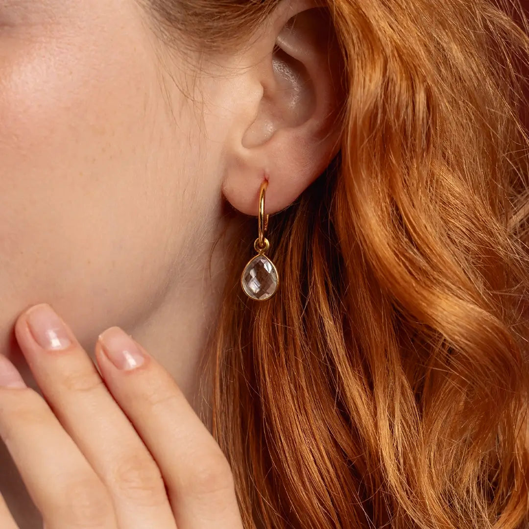 Close-up of gold drop hoop earring with faceted white quartz gemstone