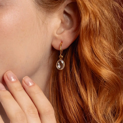Close-up of gold drop hoop earring with faceted white quartz gemstone