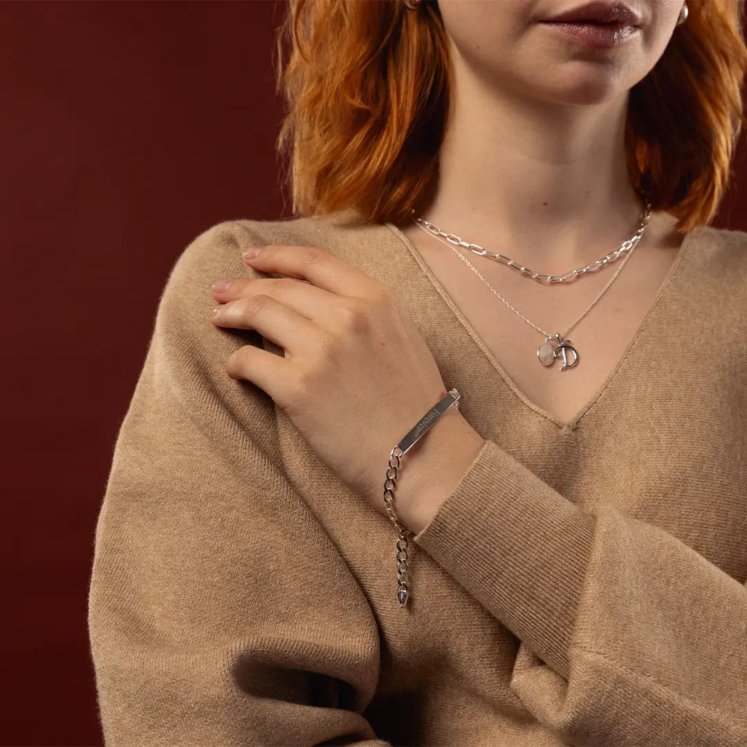 Woman wearing a sterling silver ID bracelet with Forever engraving and layered silver necklaces