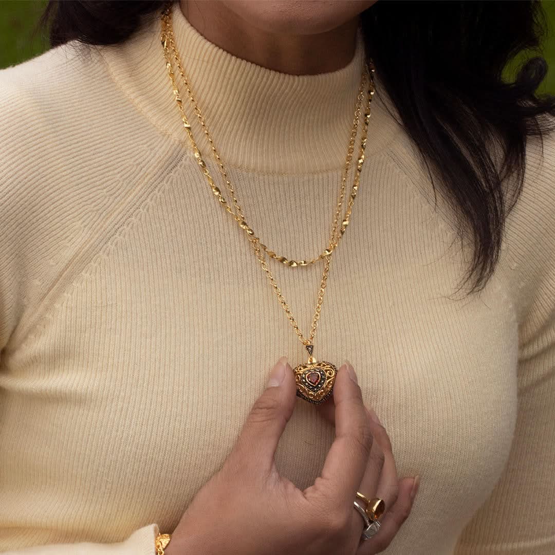 Woman wearing layered gold necklaces with ornate garnet heart locket pendant and matching gold ring