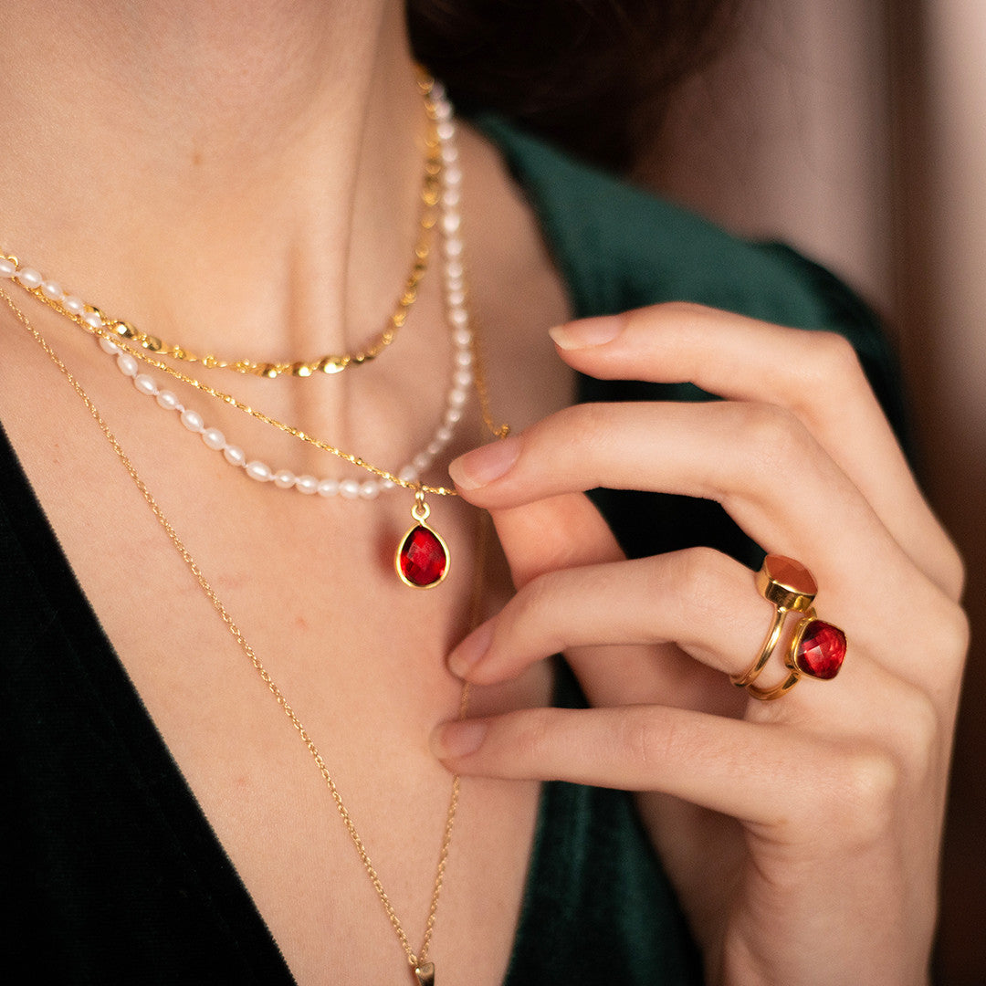 model wearing garnet cocktail ring in gold and garnet charm necklace