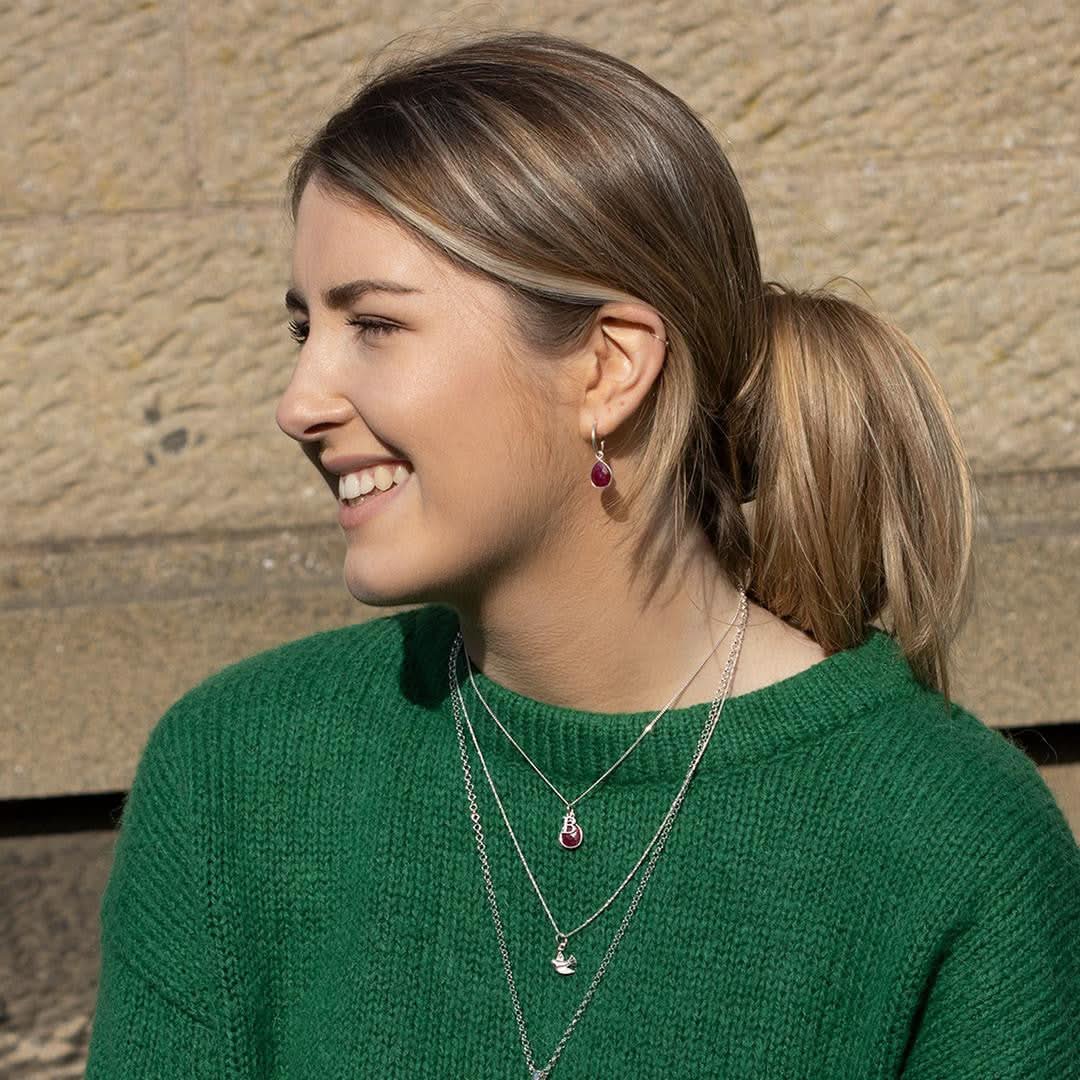 model in jumper wearing silver necklace and hoop earring with ruby gemstone charms