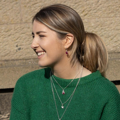 model in jumper wearing silver necklace and hoop earring with ruby gemstone charms