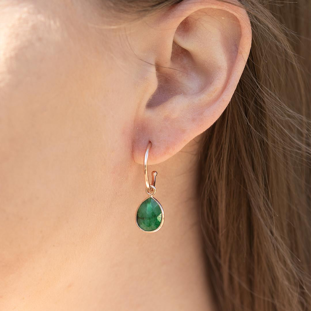 closeup of model wearing emerald drop hoop earrings in rose gold