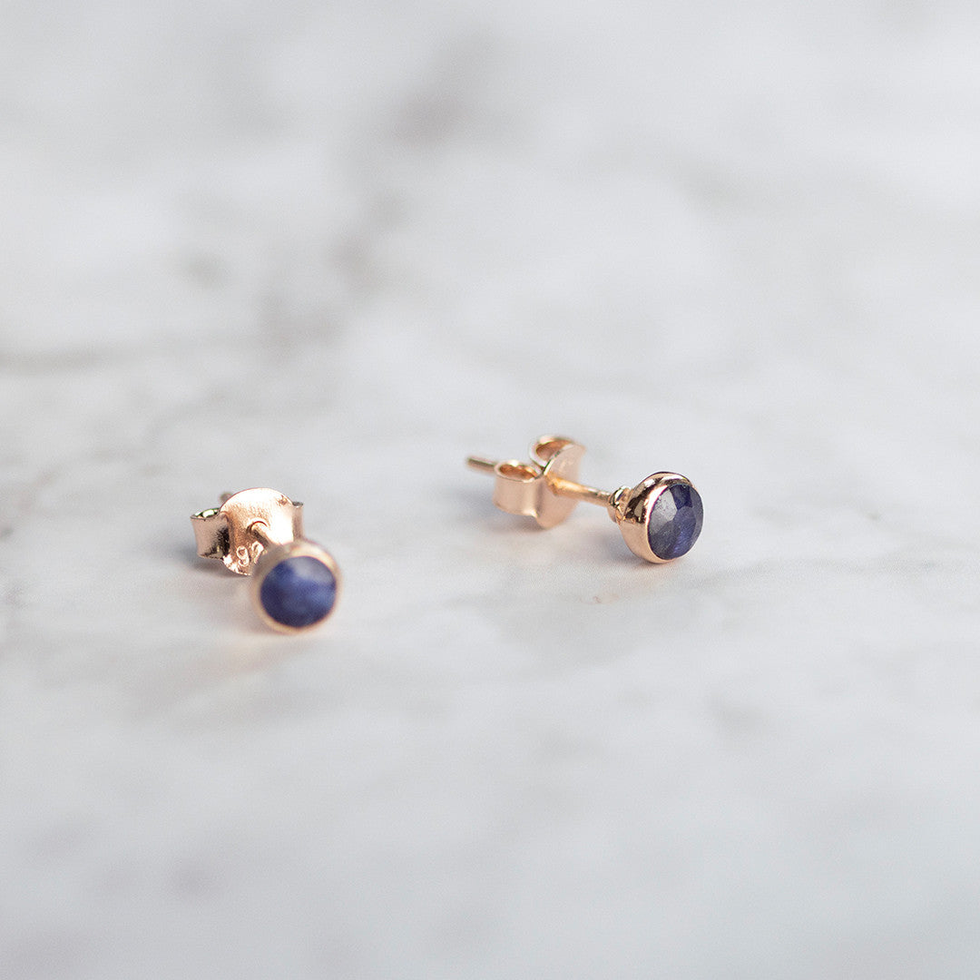 Sapphire mini stud earrings in rose gold laid out on a marble surface
